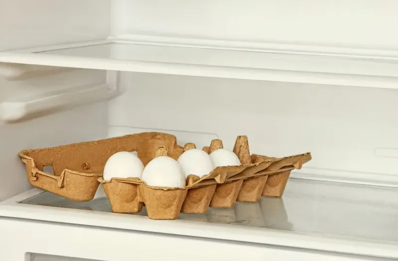 Fresh eggs in a paper box on refrigerator shelf.
